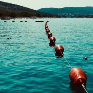 Calm water scene with red buoys forming a line across the tranquil sea and scenic hills.